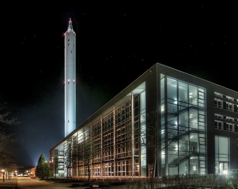 In einem Nachtmotiv ist ein großer Turm und ein großes, modernes Universitätsgebäude zu sehen. 