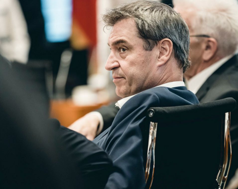 Ein Mann mit graumelierten Haaren ist von der Seite in den Reihen eines Sitzungssaals zu sehen mit angespannter Miene. Es ist Ministerpräsident Markus Söder. 