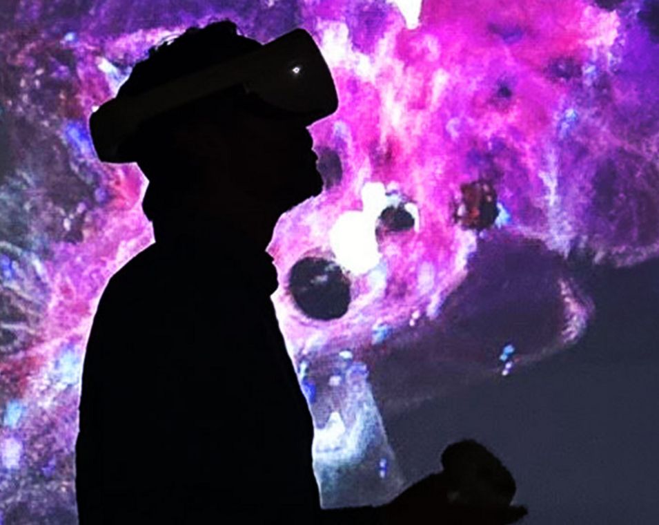 In einem dunklen Raum mit lila anmutenden Lichtwolken sieht man die Silhouette einer Person mit Virtual-Reality-Brille. 