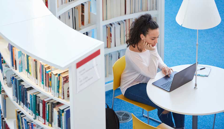 Eine junge Frau sitzt am Laptop in einer Bibliothek