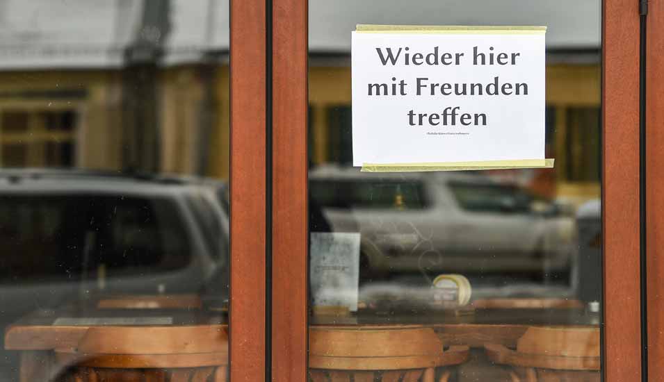 Am Fenster einer Bar in Friedrichshagen hängt ein Schild mit der Aufschrift "Wieder hier mit Freunden treffen". Durch das Fenster kann man leere Stühle und Tische sehen. 