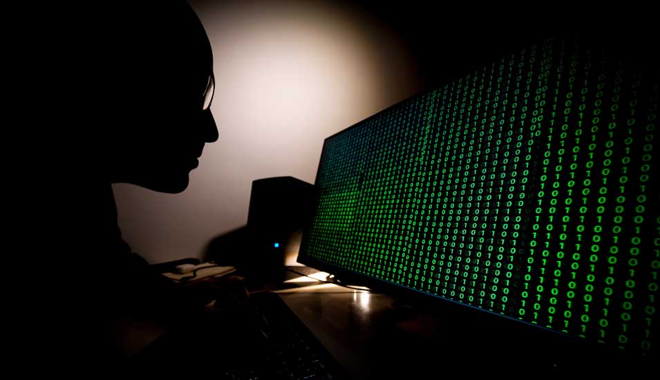 Ein Mann sitzt im Dunkeln vor einem Computerbildschirm mit binärem Code.