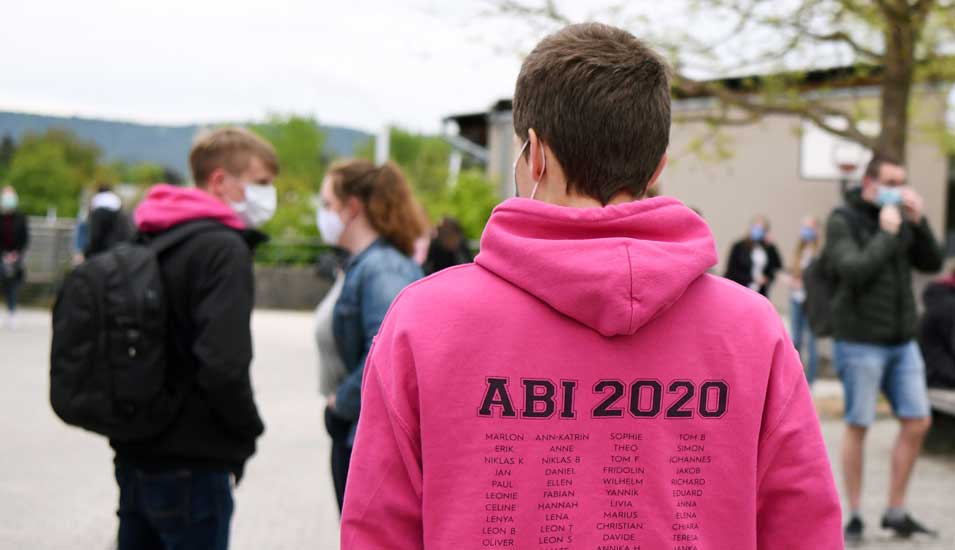Abiturienten mit Mund-Nasen-Schutz und Pullover mit der Aufschrift "Abi 2020"