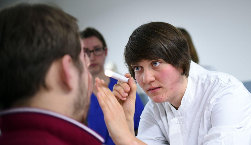 Das Foto zeigt eine Medizinstudentin, die bei einer Simulation eine Auge untersucht.