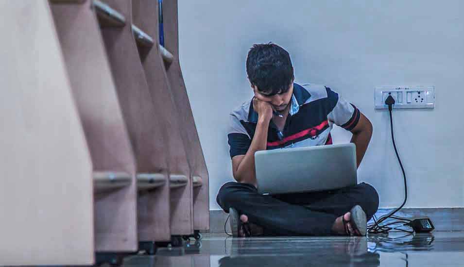 Schüler oder Student sitzt mit einem Laptop auf dem Boden in einer Bibliothek