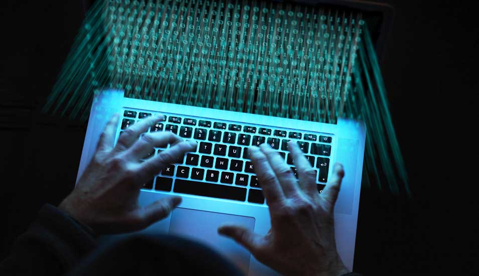 Das Foto zeigt Hände auf einer Laptoptastatur in einem dunklen Raum.