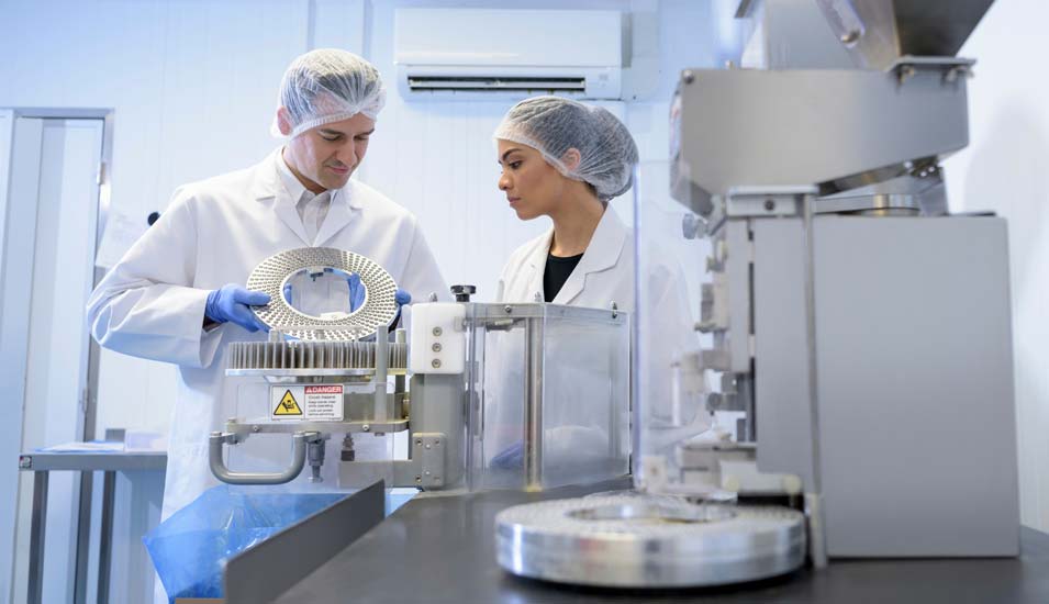 Zwei Mitarbeiter arbeiten an einer Maschine in einer pharmazeutischen Fabrik