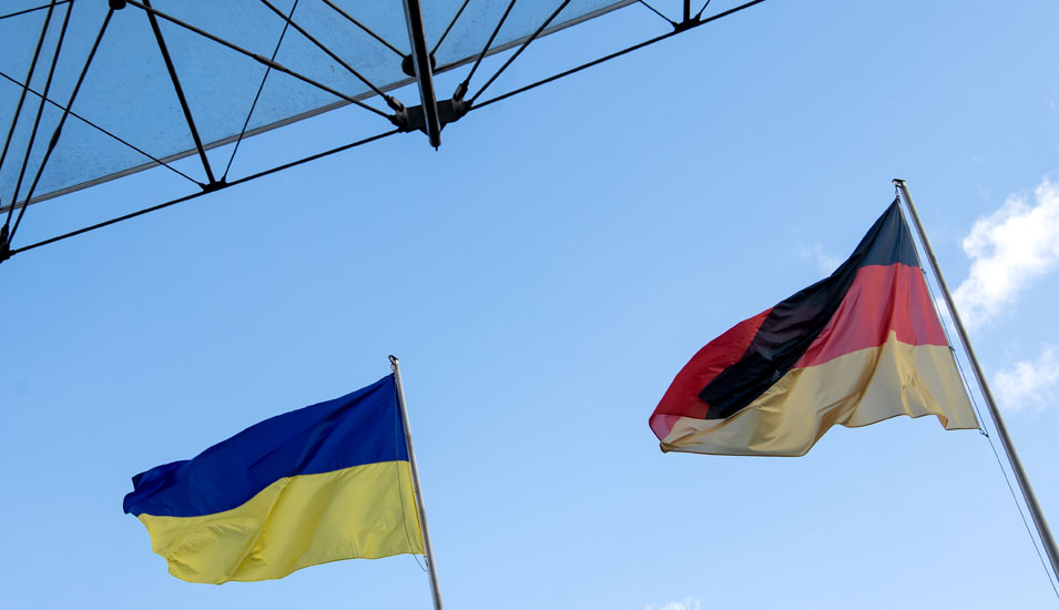 Ukrainische und deutsche Flagge vor blauem Himmel im Hintergrund.