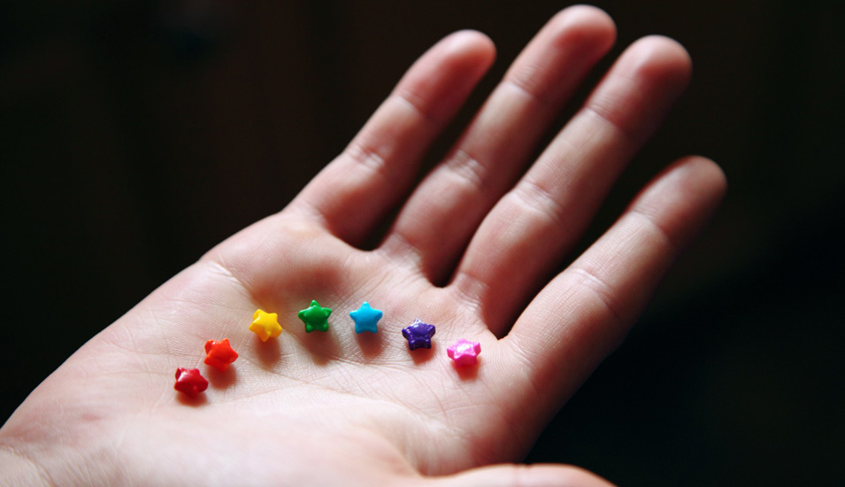 Auf einer Hand sind bunte Plastisternchen in den Farben des Regenbogens zu sehen. 