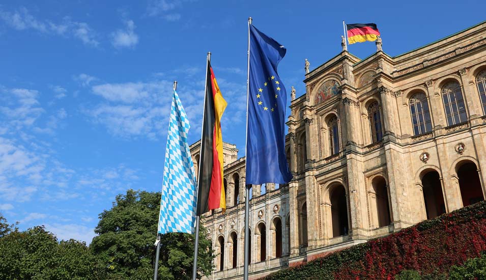 Ein historisches Gebäude mit der bayerischen, deutschen und europäischen Flagge davor. 