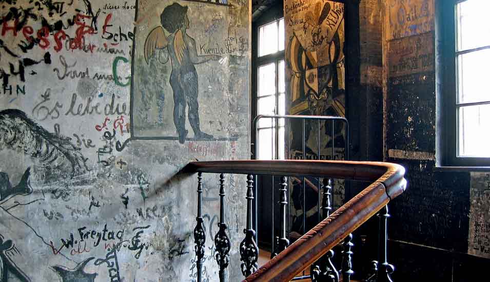 Das Bild zeigt einen Blick ins Treppenhaus des Heidelberger Karzers. Die Wände sind über und über mit Malereien und Inschriften verziert.