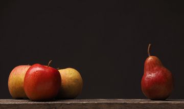 Drei rote Äpfel und daneben eine rote Birne vor dunklem Hintergrund.