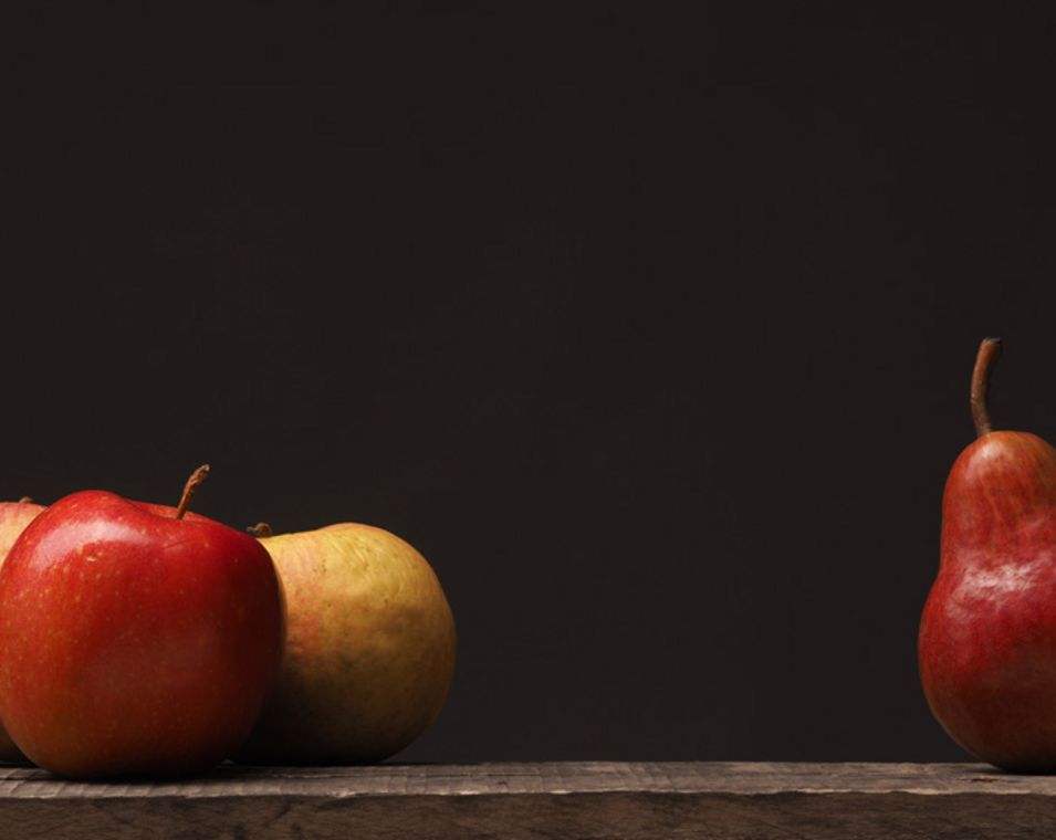 Drei rote Äpfel und daneben eine rote Birne vor dunklem Hintergrund.