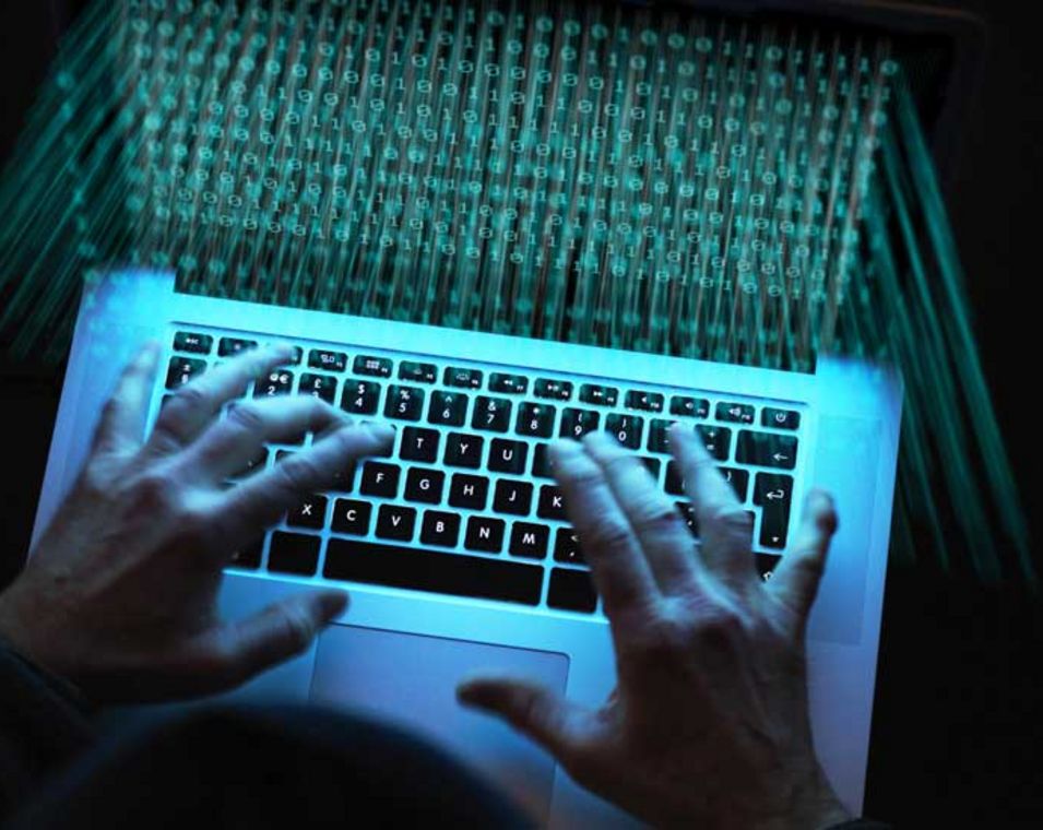 Das Foto zeigt Hände auf einer Laptoptastatur in einem dunklen Raum.