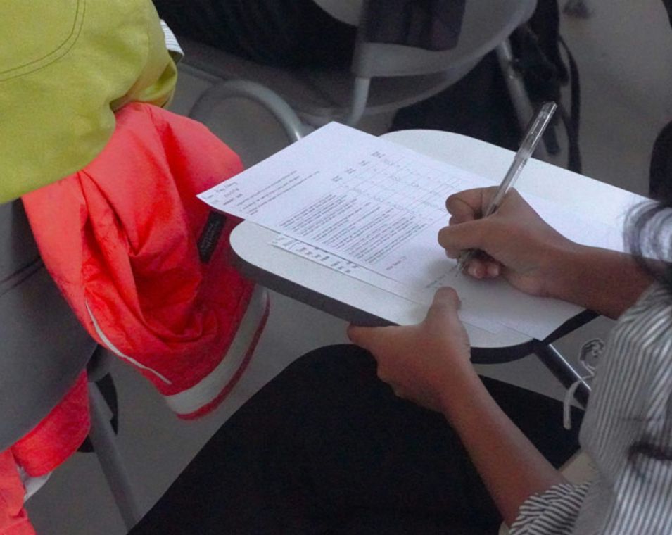 Eine junge Frau beantwortet auf einem Blatt vor ihr auf einem Desk Prüfungsfragen. 