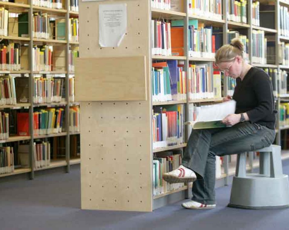Das Foto zeigt eine Studentin vor einem Bücherregal in der Universitätsbibliothek Jena.
