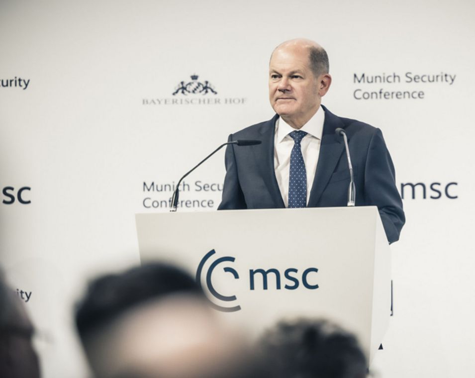 Vor einer weißen Wand mit der Aufschrift "Münchner Sicherheitskonferenz" ist Bundeskanzler Olaf Scholz in ein Mikrofon sprechend zu sehen.