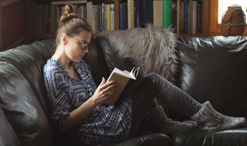 Das Foto zeigt eine lesende Frau auf einem Sofa im Wohnzimmer