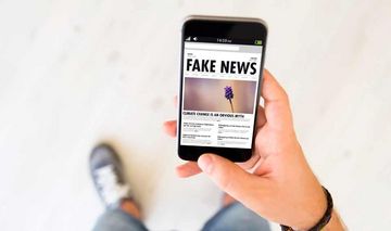 Hand einer Person, die auf dem Smartphone Fake News liest