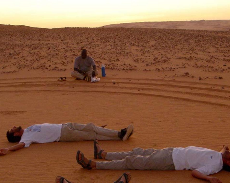 Forscherteam liegt am Abend auf dem Boden in der Wüste