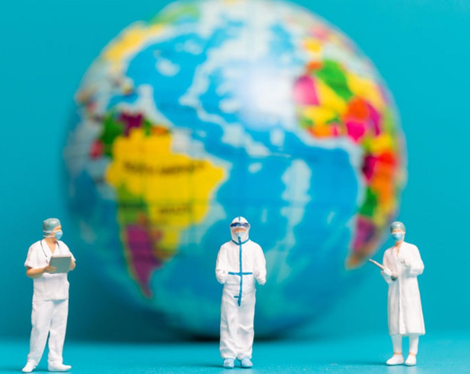 Drei Spielfiguren in ärztlicher Kleidung stehen vor einem unscharfen Globus