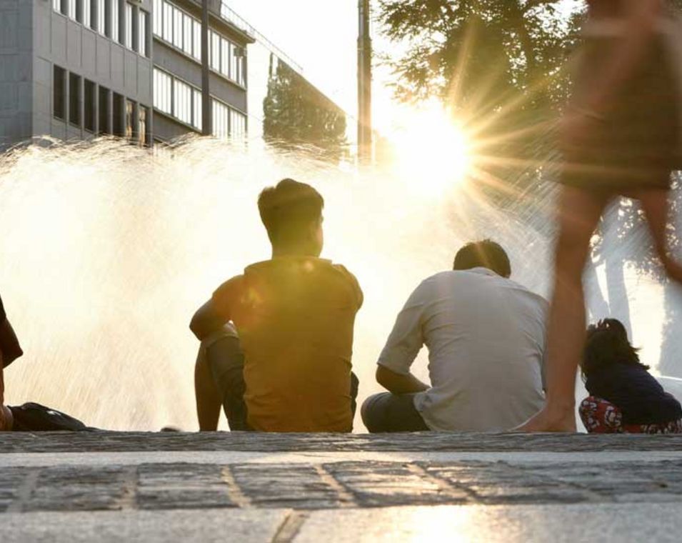 Menschen sitzen im Sommer bei Sonnenuntergang am Münchner Stachusbrunnen