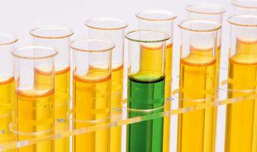 Das Foto zeigt eine Reihe mit Reagenzgläsern, die mit gelber und eines mit grüner Flüssigkeit gefüllt sind
