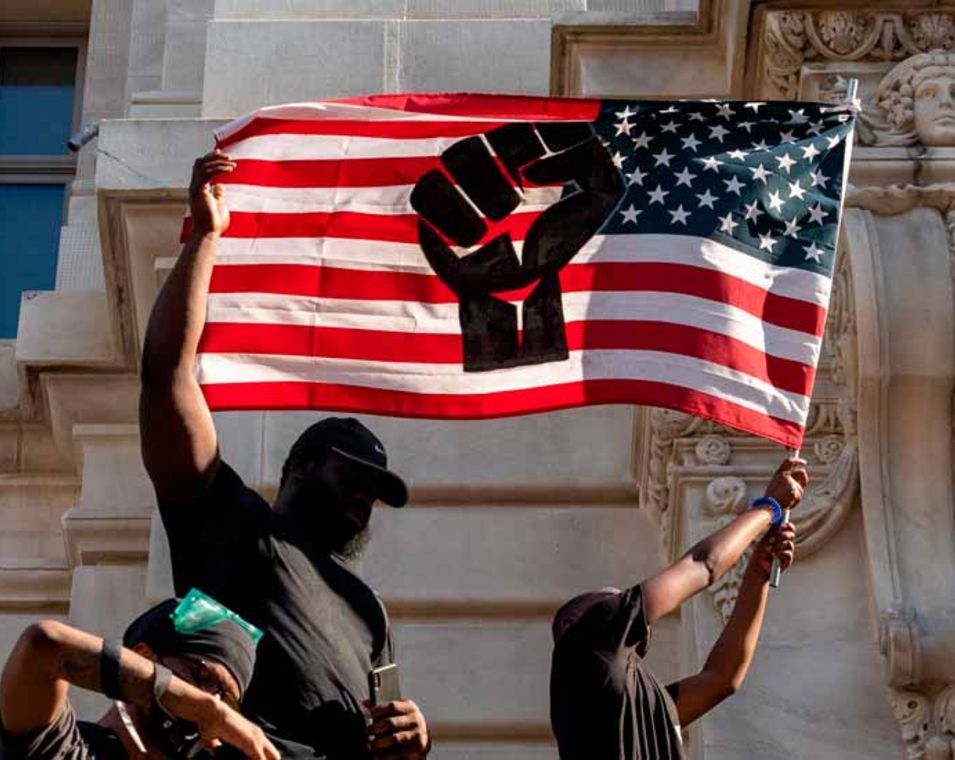 Schwarze Protestanten schwenken eine USA-Flagge mit einem Faussymbol gegen Rassismus