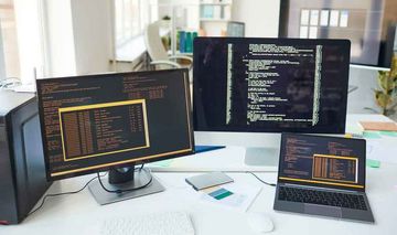 mehrere Bildschirme mit Programmierungscode einer Software in einem Büroraum