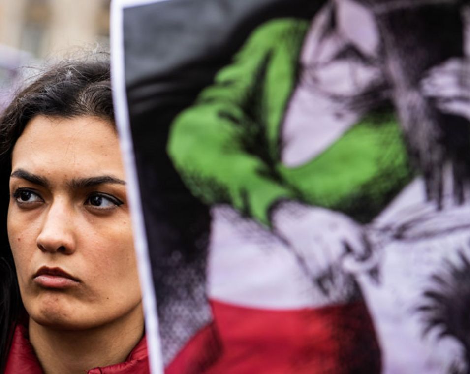 Im Oktober demonstriert eine junge Frau in Paris und hält ein Plakat hoch auf dem eine gezeichnete Frau gekleidet in den Farben der iranischen Flagge ihre Haare abschneidet.