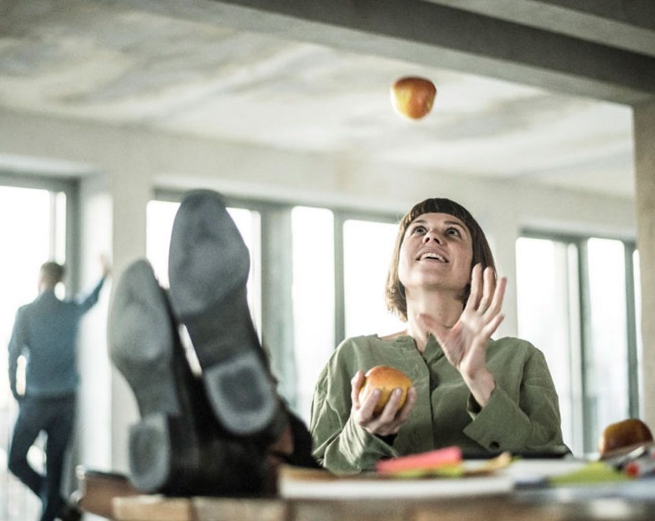 Eine Frau jongliert im Büro mit zwei Äpfeln