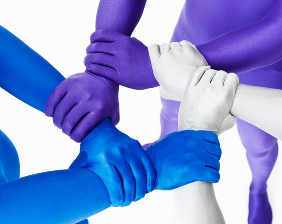 Einheit in Vielfalt: Hände in unterschiedlichen Blau- und Lilatönen umfassen einander, sodass sie einen Stern bilden.