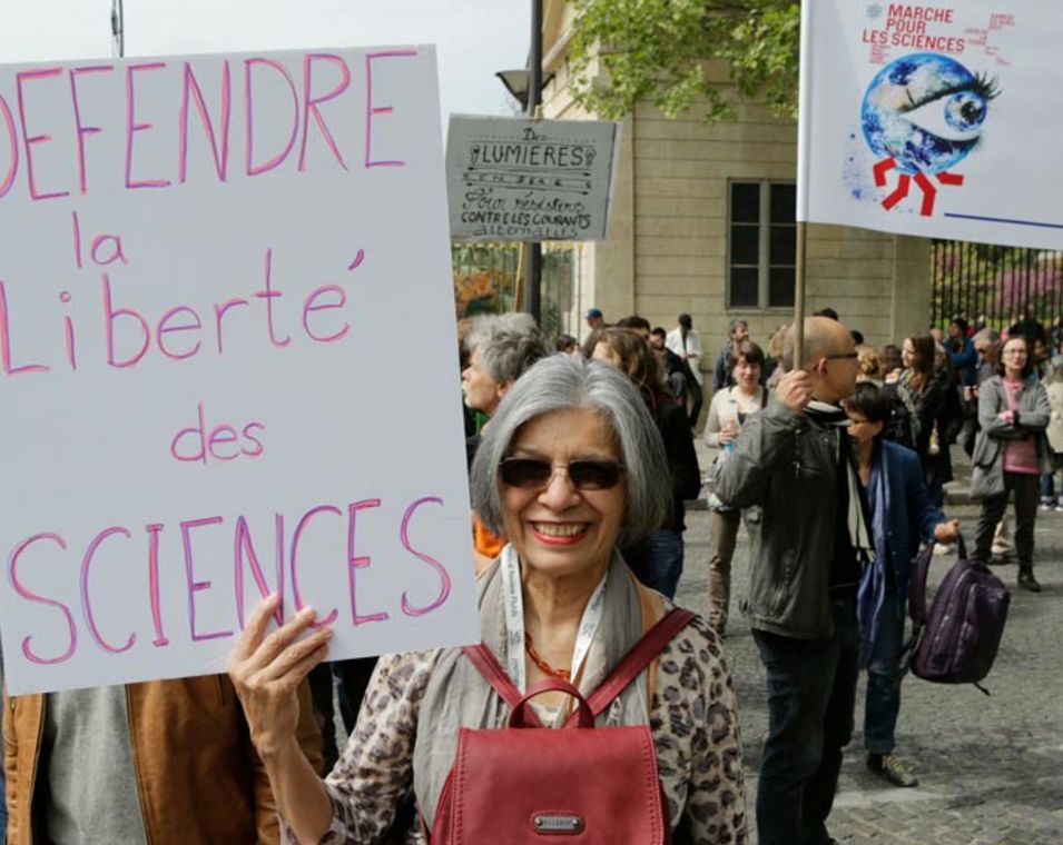 Eine Demonstrantin hält ein Schild mit französischer Schrift hoch mit der Forderung, die Wissenschaftsfreiheit zu schützen. 
