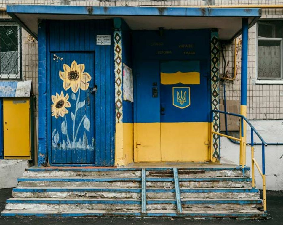 Eine Häuerfront samt Tür ist in den ukrainischen Nationalfarben bemalt. Eine Sonnenblume ziert zudem eine Tür. 