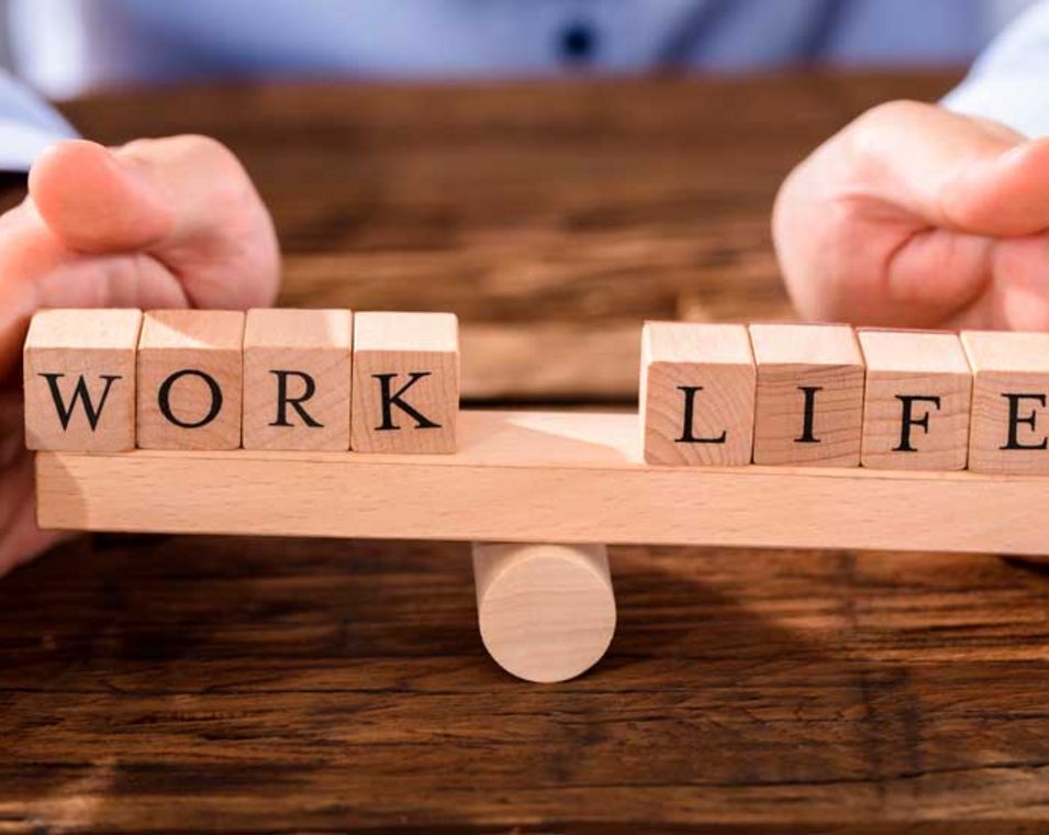Eine Person gewichtet auf einer Waage Holzklötze zum Thema "Work" und "Life".