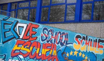Schriftzug "Schule" in verschiedenen Sprachen und den Farben der jeweiligen Länder, auf dem Gelände einer Schule in Mühlheim-Broich.