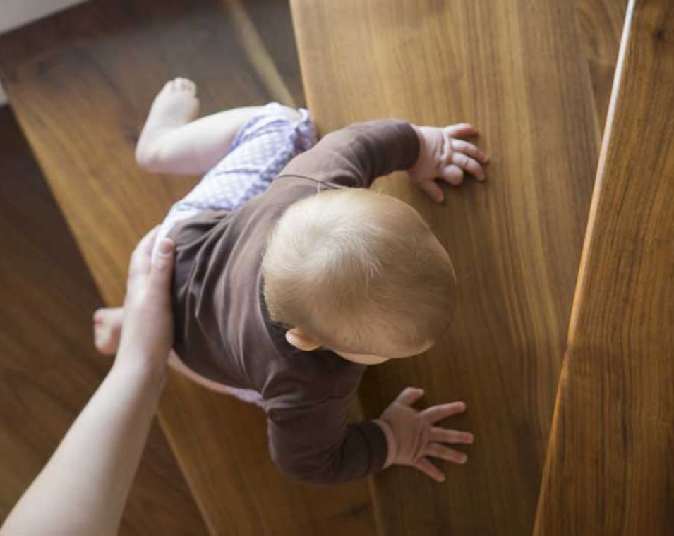 Ein Kind krabbelt mit Hilfe eines Elternteils eine Treppe hoch