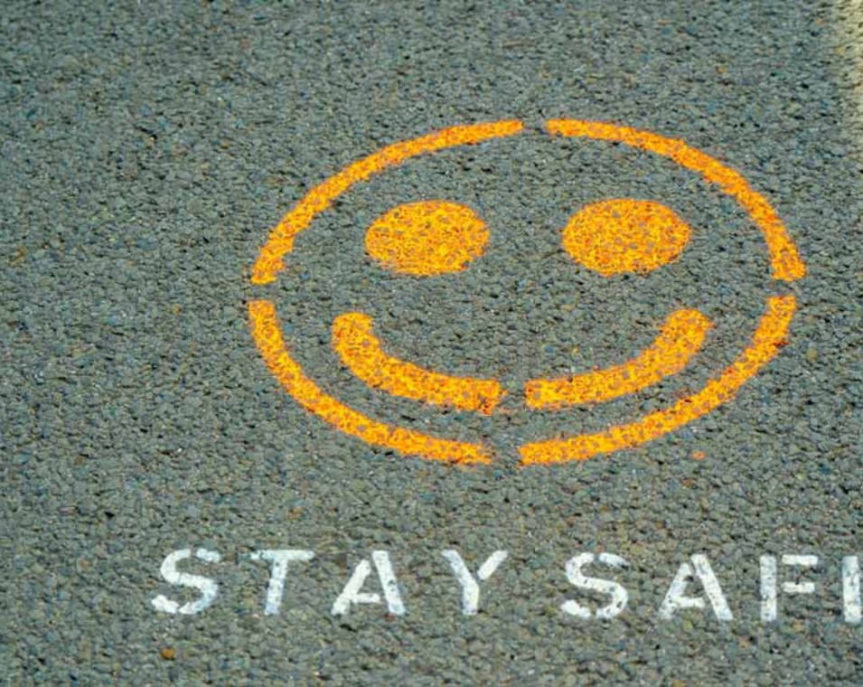 Unter einem gelben Smiley auf Asphalt steht "Stay Safe". 