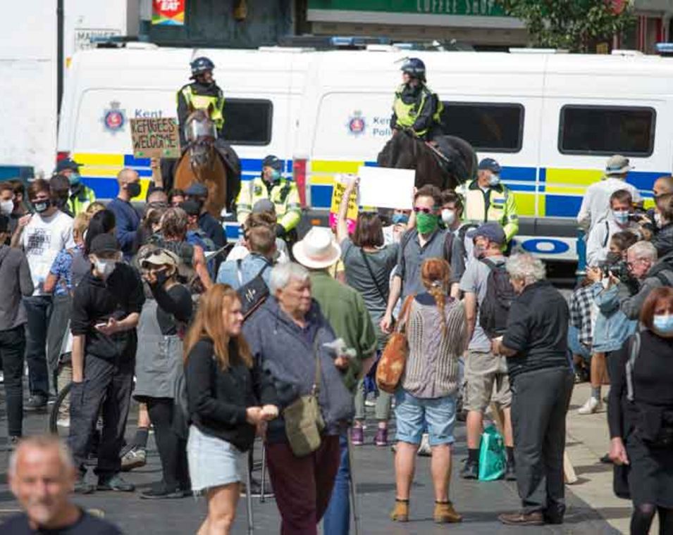 Migrationsgegner und Migrationsbefürworter stoßen bei Protesten in Dover, England aufeinander, im Bildhintergrund stehen Polizisten.