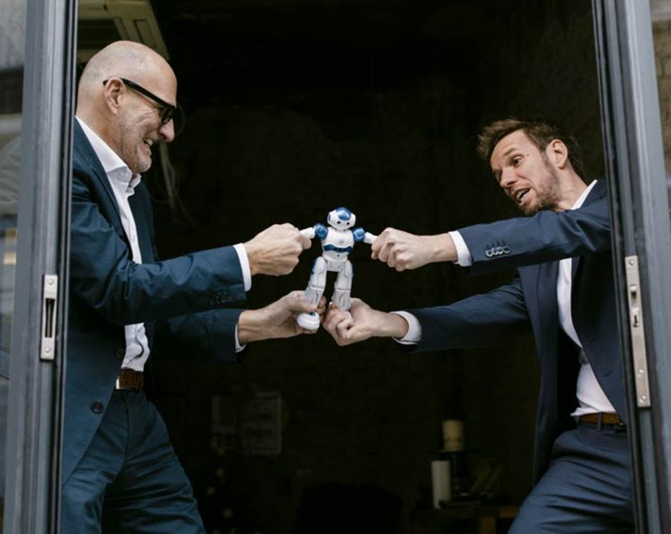 zwei Männer in Anzügen streiten sich um einen kleinen Roboter