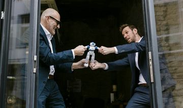 zwei Männer in Anzügen streiten sich um einen kleinen Roboter