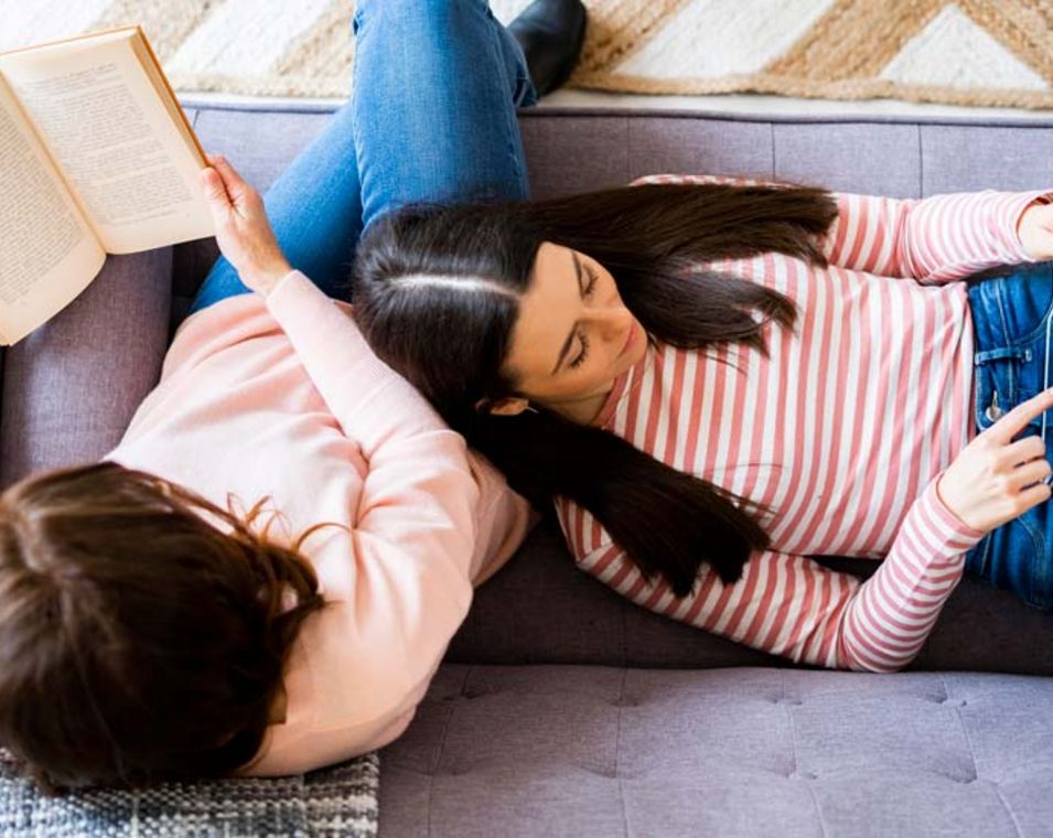 Zwei Frauen lesen auf dem Sofa, eine ein Buch, eine am Tablet