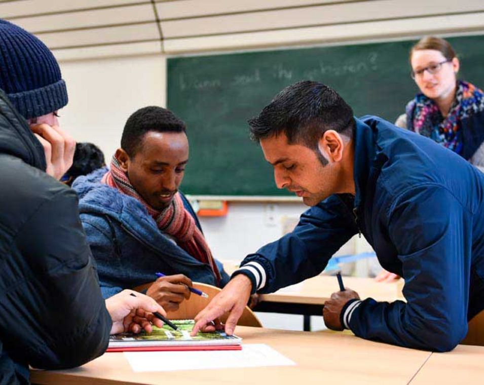 Drei Männer mit Migrationshintergrund beugen sich über ein Übungsbuch zum Deutschlernen