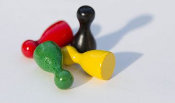 Das Foto zeigt vier verschiedenfarbige Spielfiguren, drei liegend, eine stehend.