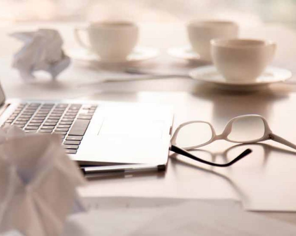 Arbeitsplatz mit Laptop, mehreren Tassen Kaffee, einer Brille und zerknülltem Papier