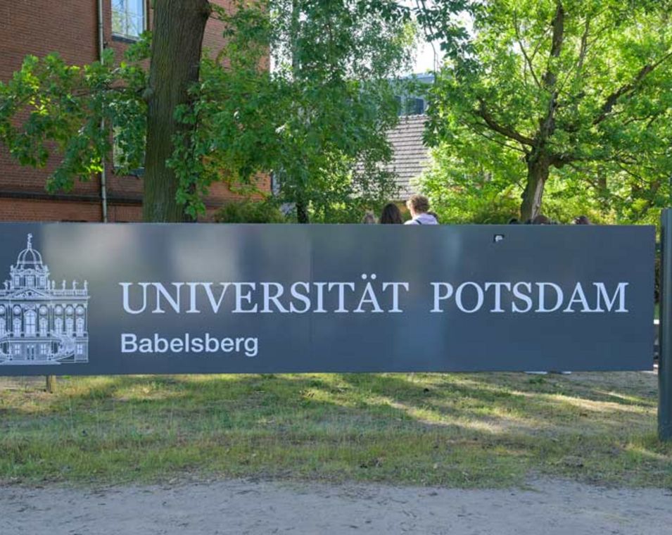 Namensschild der Universität Potsdam vor einem sandsteinfarbenen Gebäude