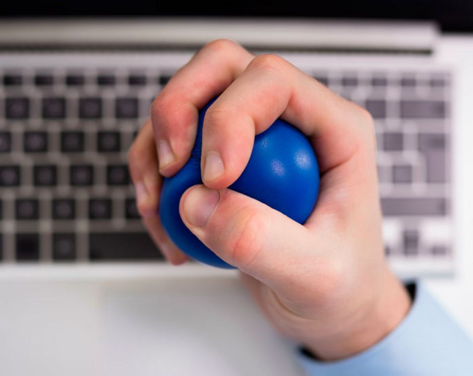 Männliche Hand, die Stressball drückt, im Hintergrund eine Computertastatur.