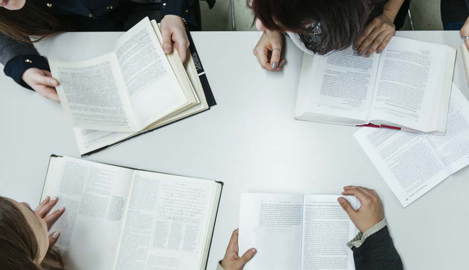 Das Foto zeigt vier Studierende mit aufgeschlagenen Büchern von oben