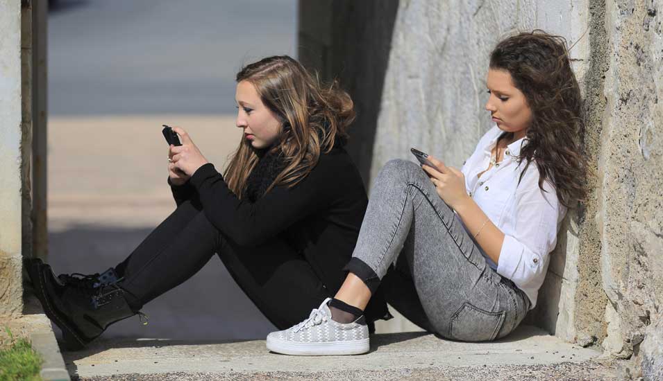 Das Foto zeigt zwei junge Frauen, die auf ihre Smartphones sehen.