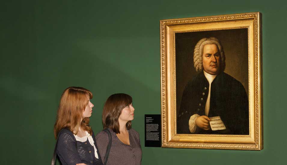 Das Foto zeigt ein Porträt Bachs in einem Museum mit zwei Besucherinnen.